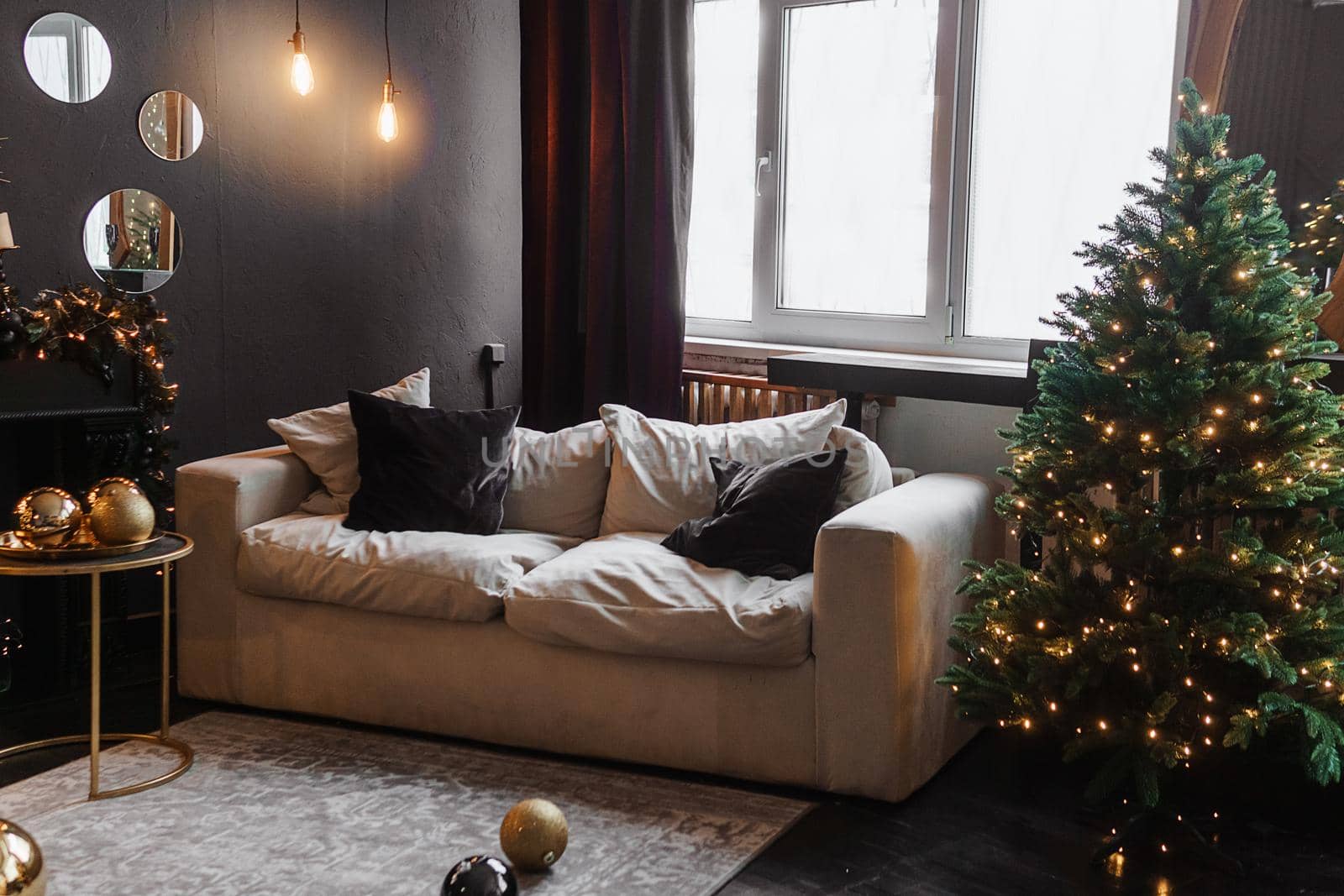 Christmas interior with a beautiful Christmas tree, sofa, light bulbs and dark background. Home New Year's interior.