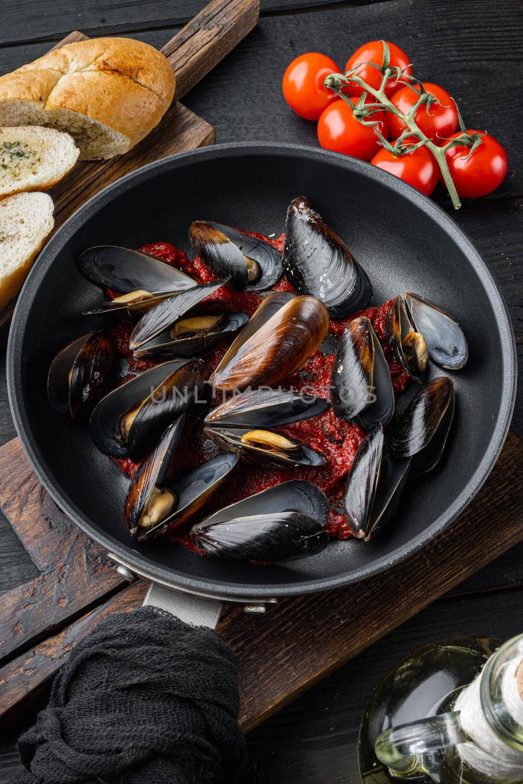 Delicious cooked seafood mussels with tomato sauce with baguette, on frying iron pan, on black wooden table background
