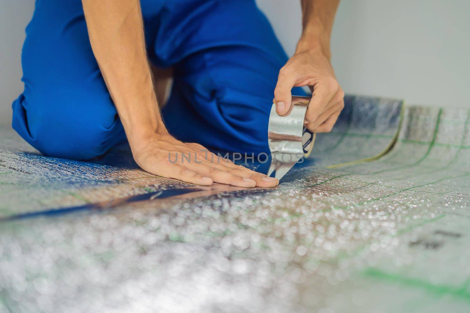 Master installs the overlapping thermal insulation in the room. Floor heating installation. Male hand holds reinforced tape. Repair in the apartment, floor insulation by galitskaya