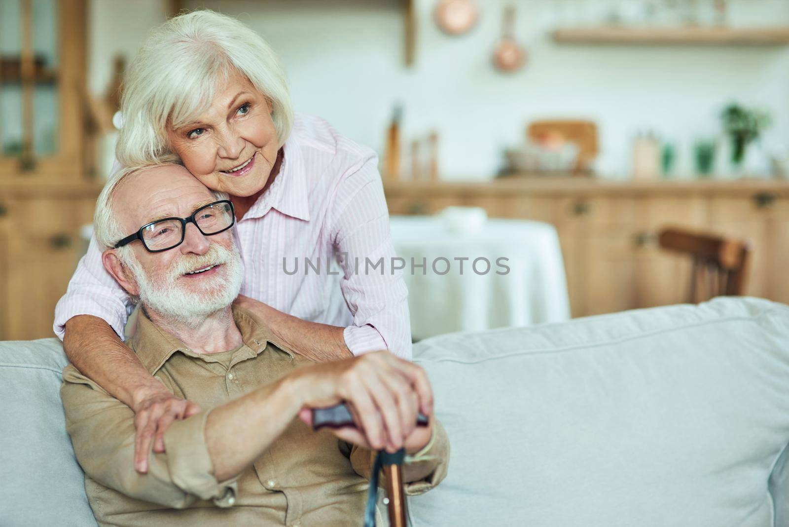 Smiling senior wife hugging her husband at home by friendsstock