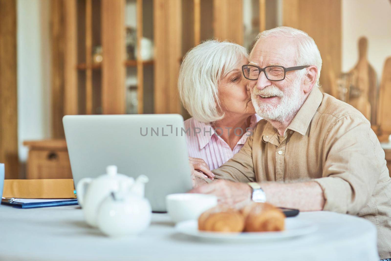 Beautiful gray-haired woman kissing her elderly husband by friendsstock