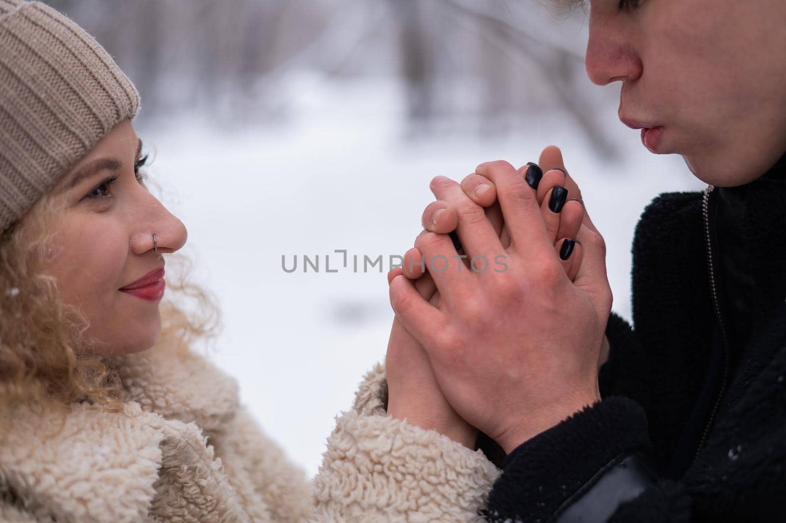 A young couple walks in the winter in the forest. The guy warms the girl's hands