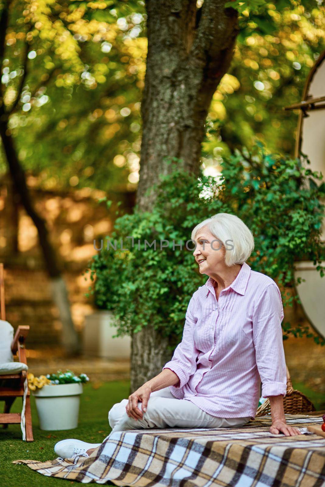 Side view of happy senior woman sitting on a blanket on the porch of the van. Lifestyle concept. Copy space
