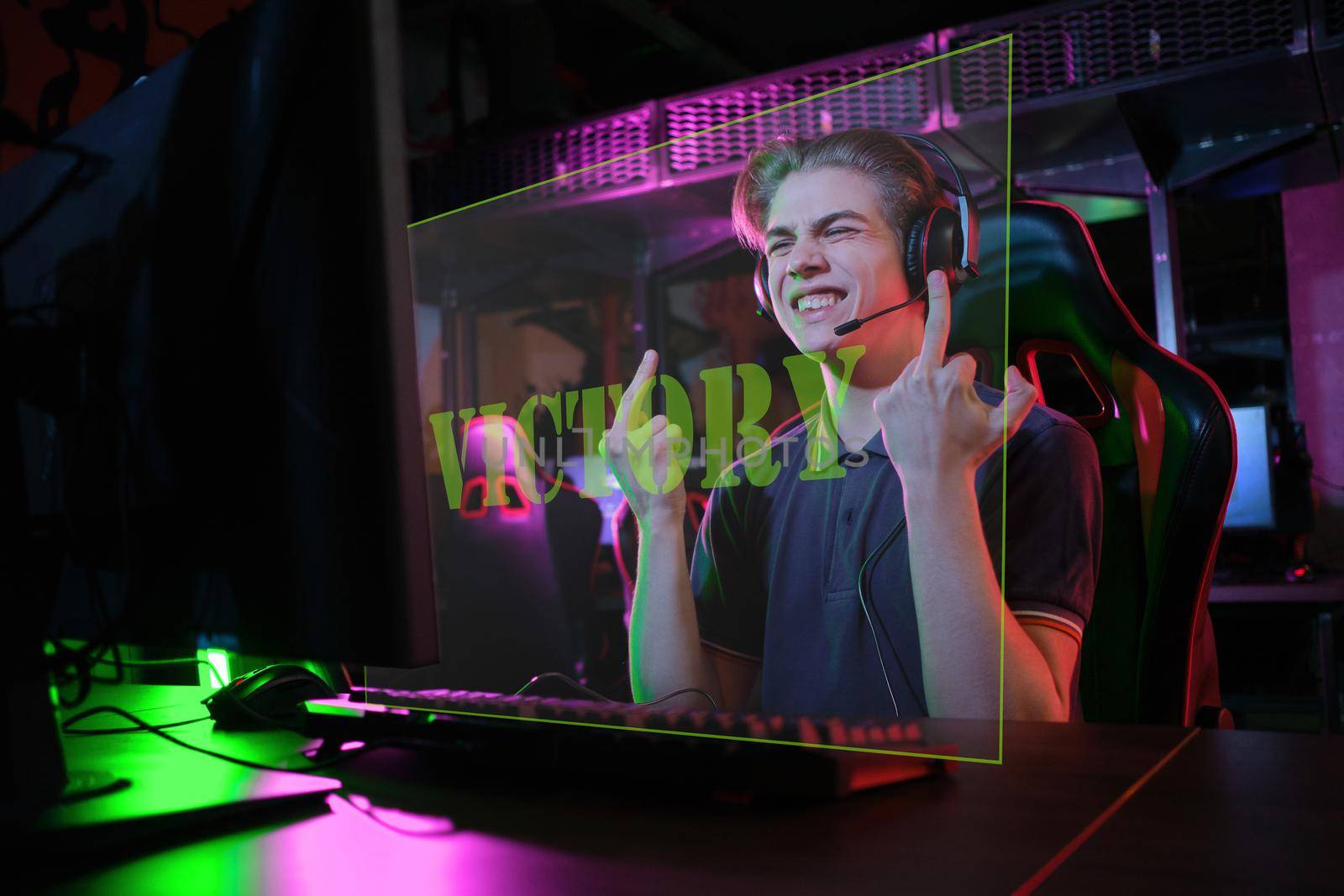 Photo of professional young caucasian gamer playing online on his PC in gaming club or cyber arena. he is upset and shows rude gestures to his virtual opponents. laser screen, projector, augmented reality, AR, VR