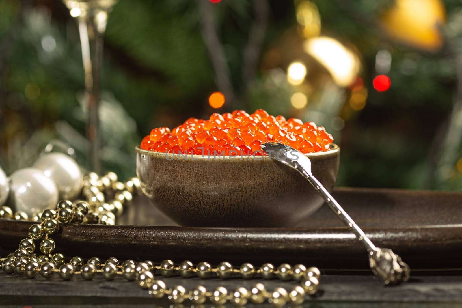 Red caviar in a a ceramic bowl, silver beads and pearlsand a glass of champagne on a silver tray. Christmas and New Year background