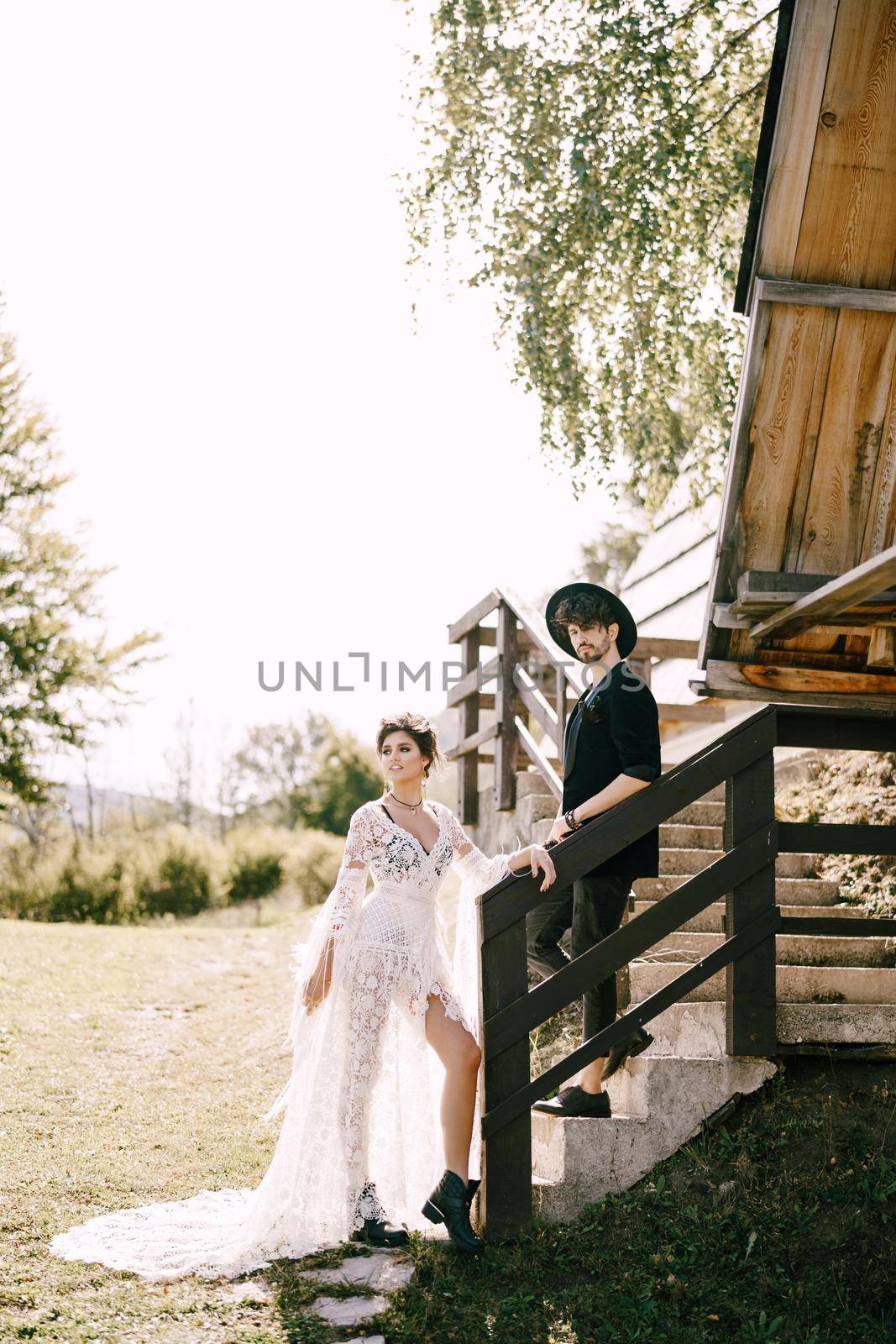 Groom and bride stand on the stone steps near the wooden hut. High quality photo