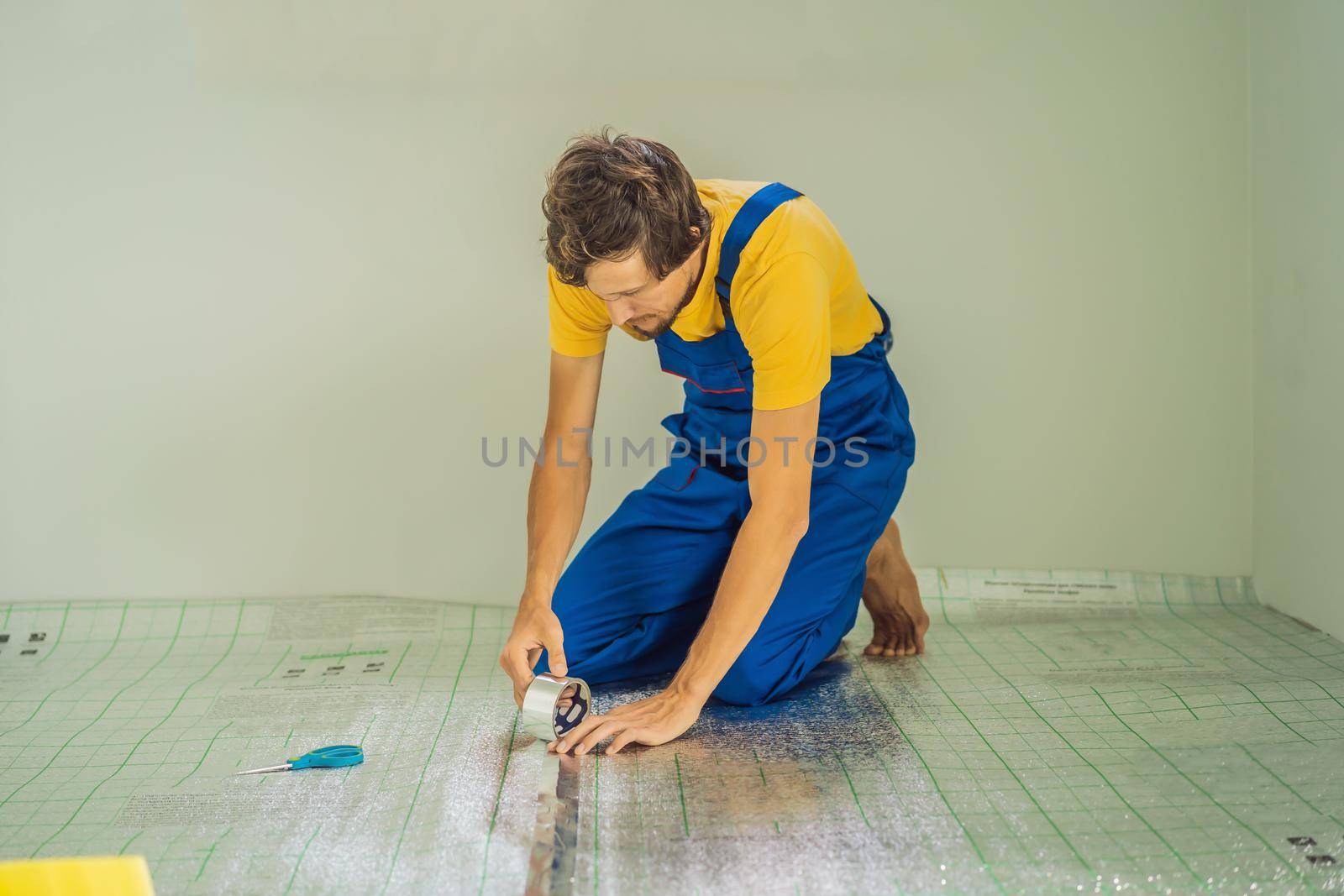 Master installs the overlapping thermal insulation in the room. Floor heating installation. Male hand holds reinforced tape. Repair in the apartment, floor insulation by galitskaya
