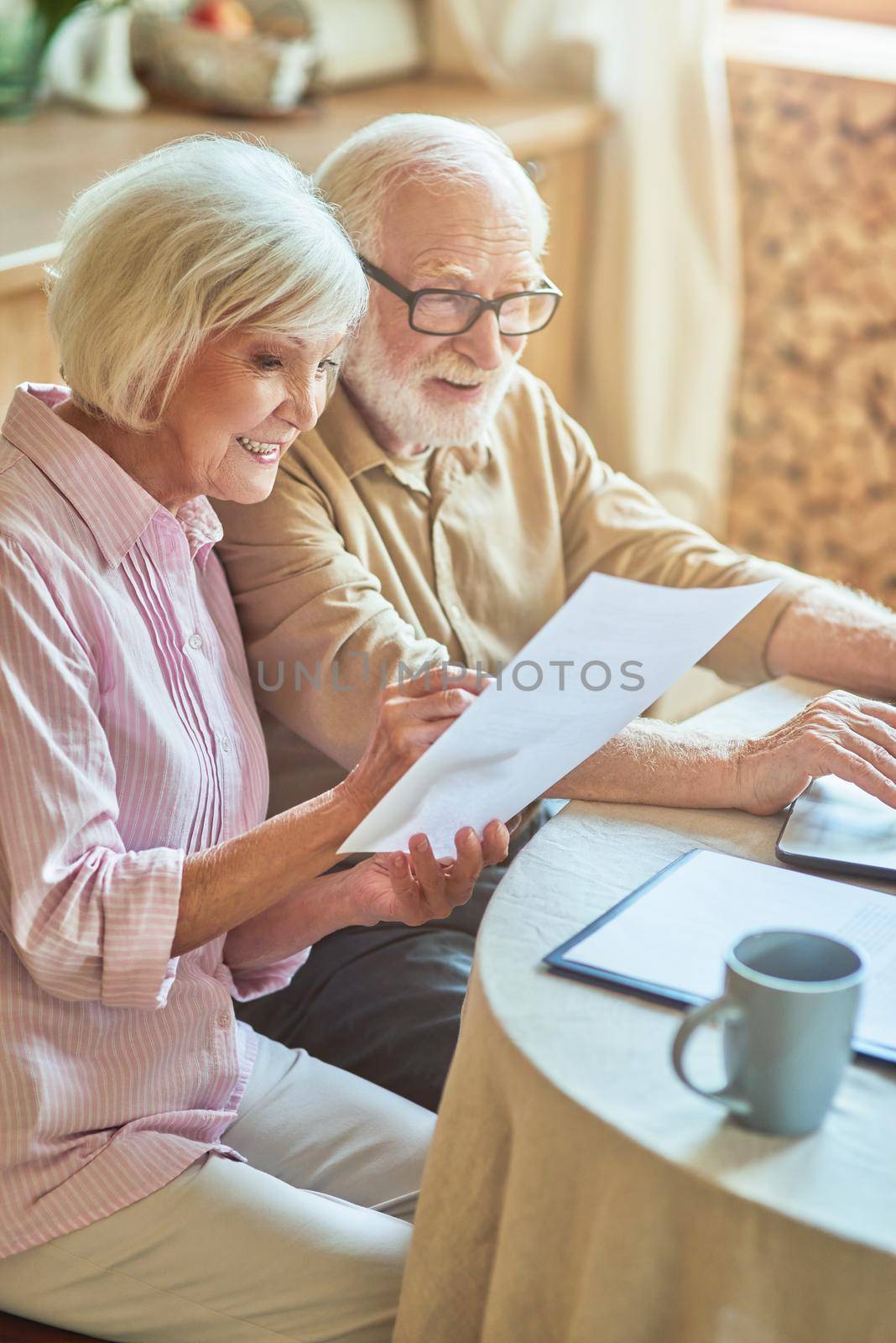 Happy senior couple with documents sitting in kitchen table at home. Family and household concept