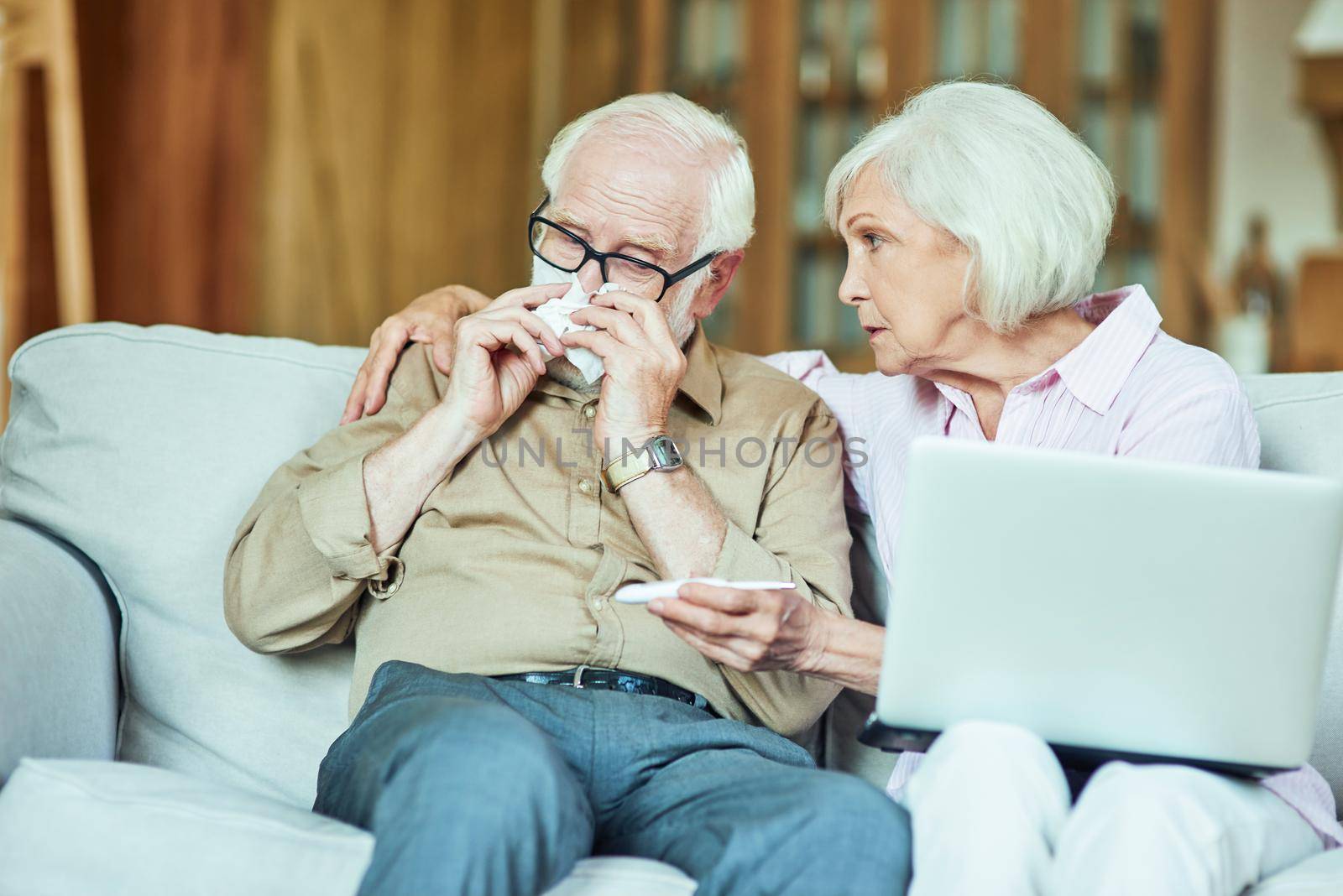 Senior wife taking care of her spouse while having online consultation at home. Care and health concept