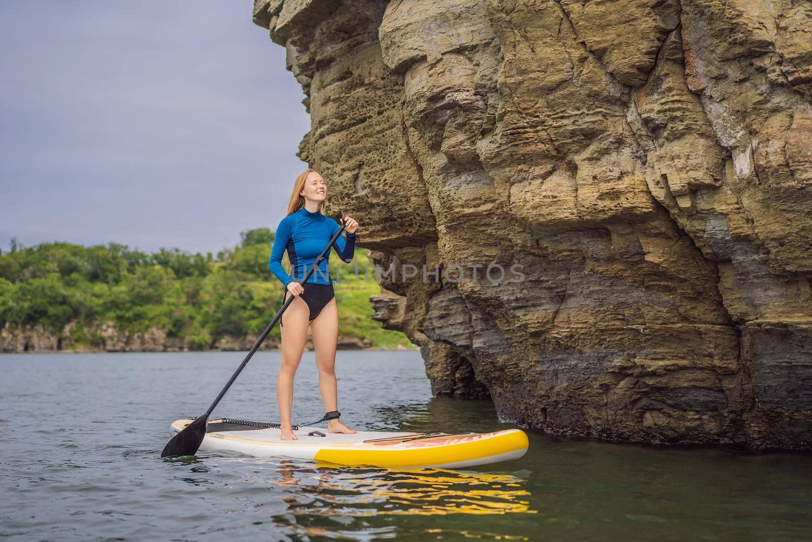 Young women Having Fun Stand Up Paddling in the sea. SUP. Red hair girl Training on Paddle Board near the rocks by galitskaya