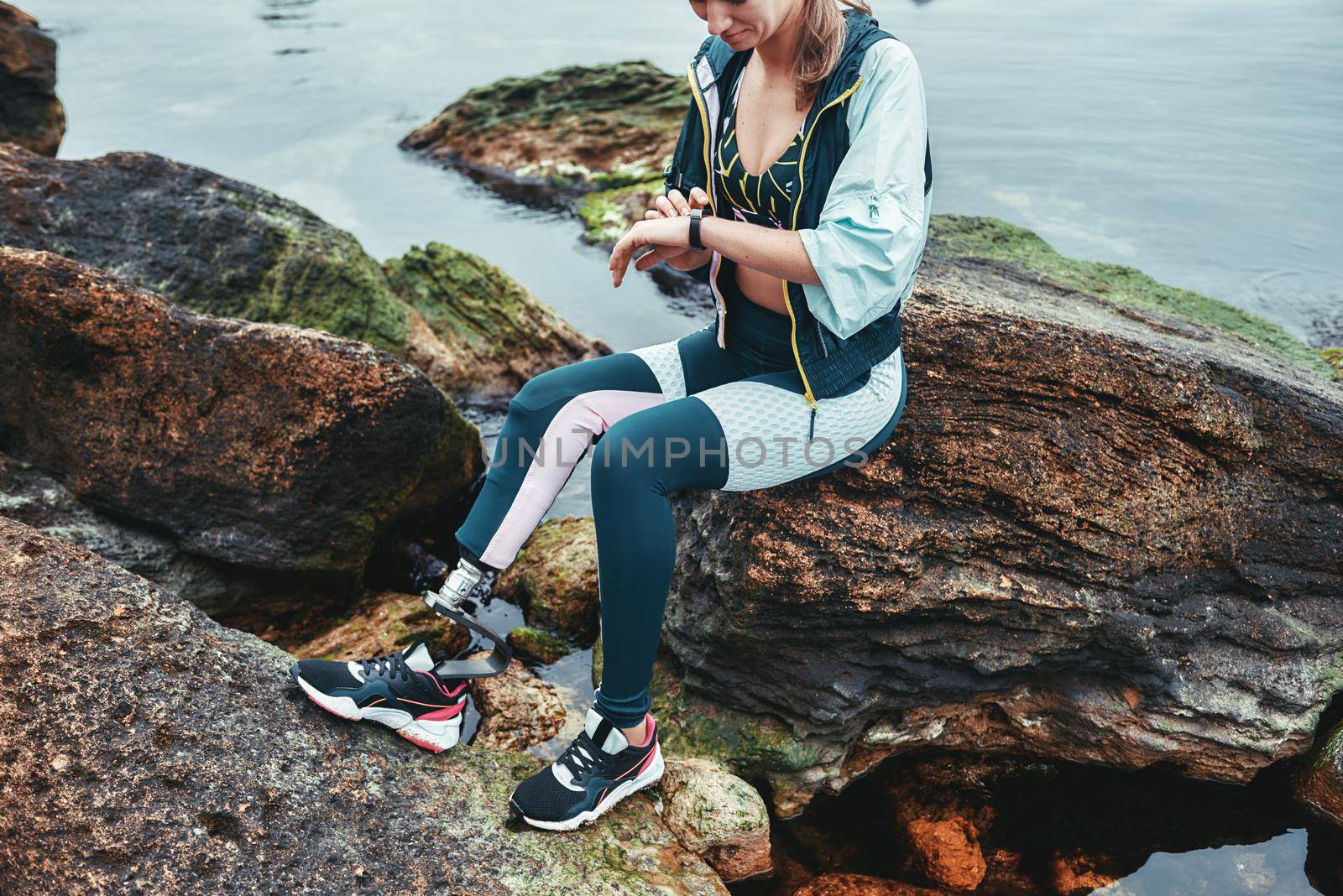 Great workout. Cropped photo of disabled athlete woman in sportswear with prosthetic leg checking results while sitting on the stone by friendsstock
