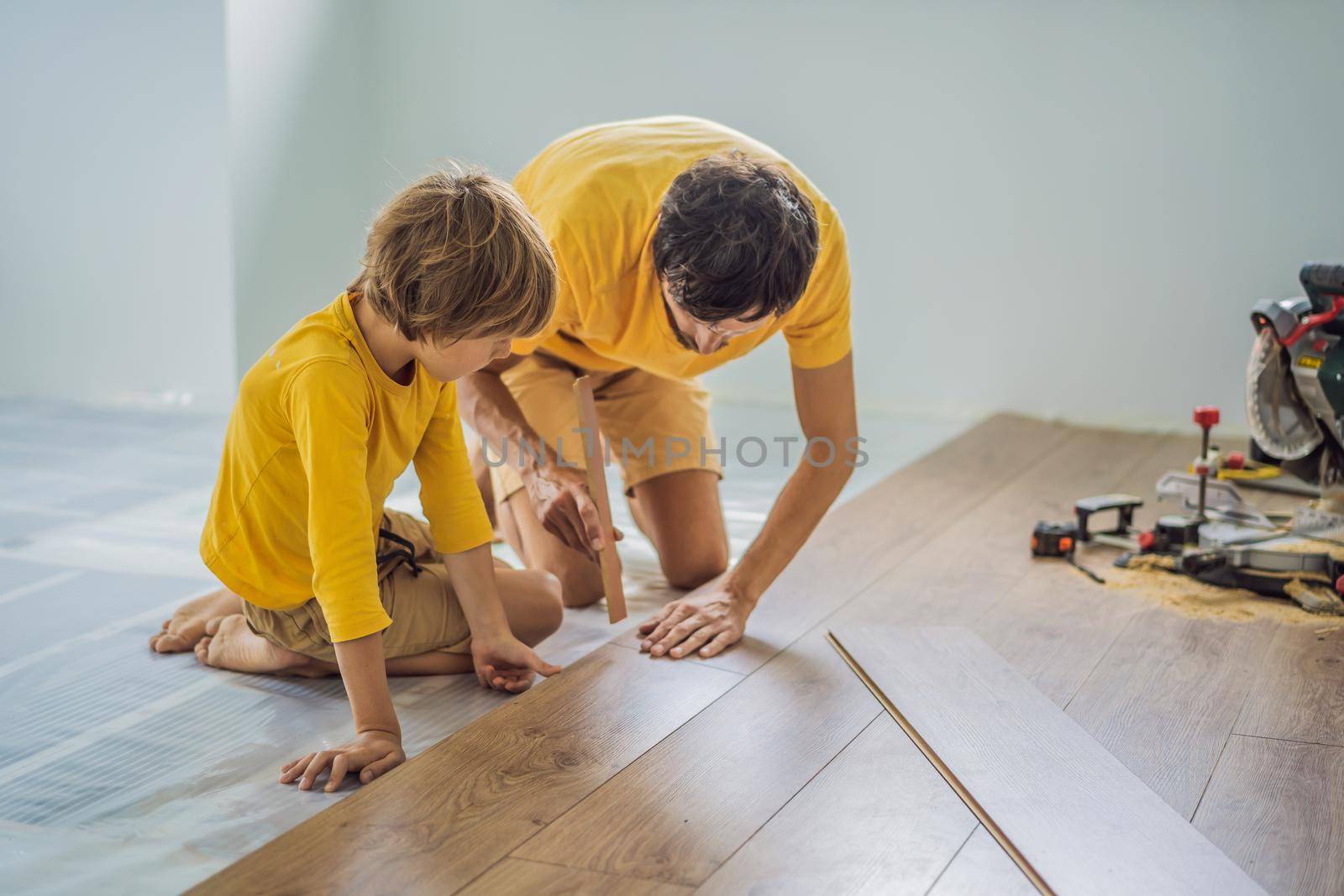 Father and son installing new wooden laminate flooring on a warm film floor. Infrared floor heating system under laminate floor by galitskaya