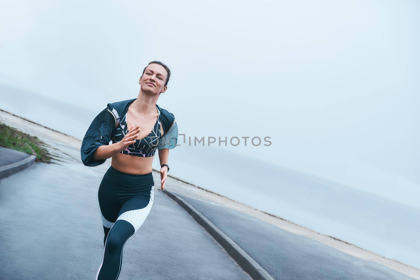 My everyday motivation. Happy and strong disabled woman in sportswear is running outdoors near the sea and smiling. by friendsstock