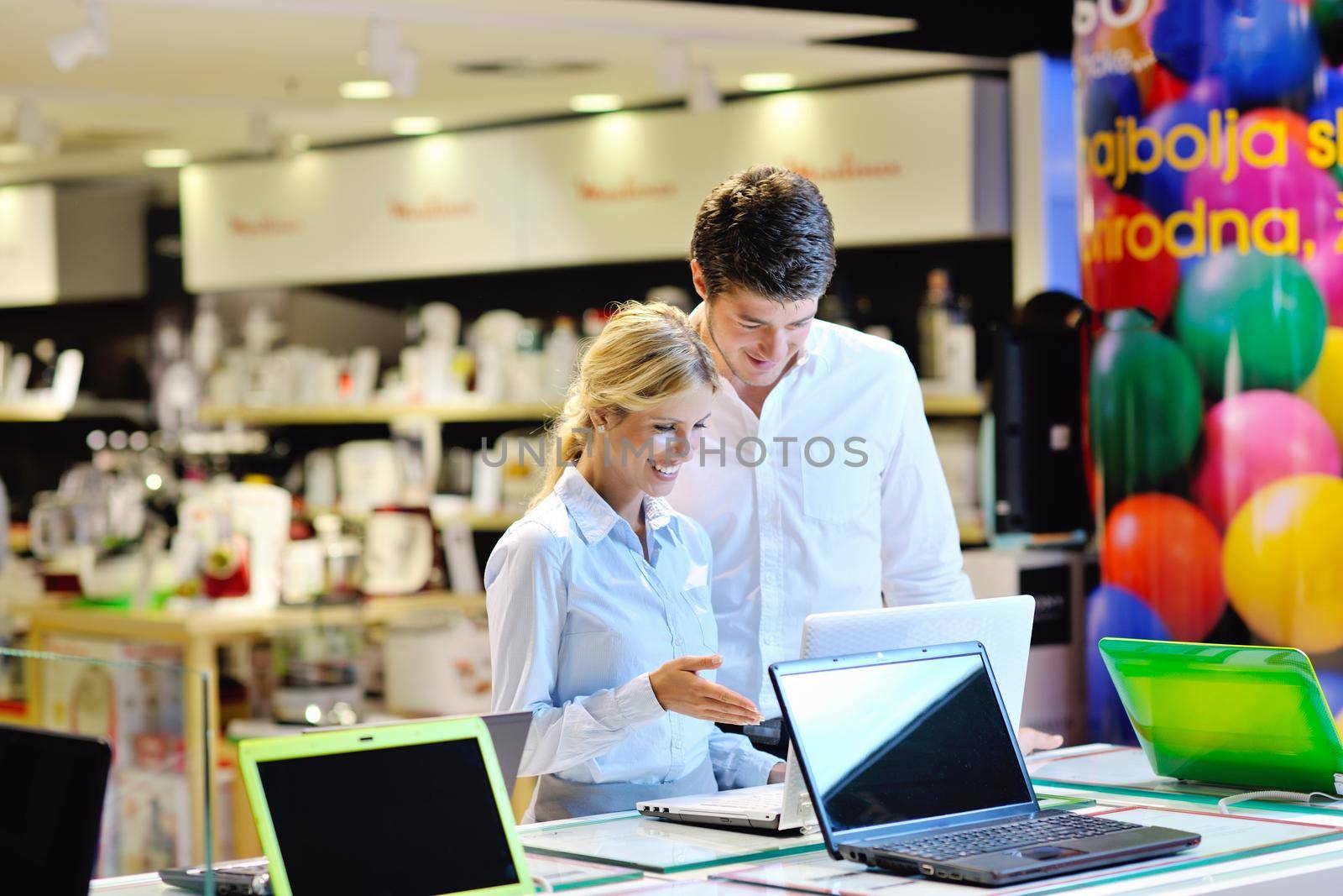 Young couple in consumer electronics store looking at latest laptop, television and photo camera