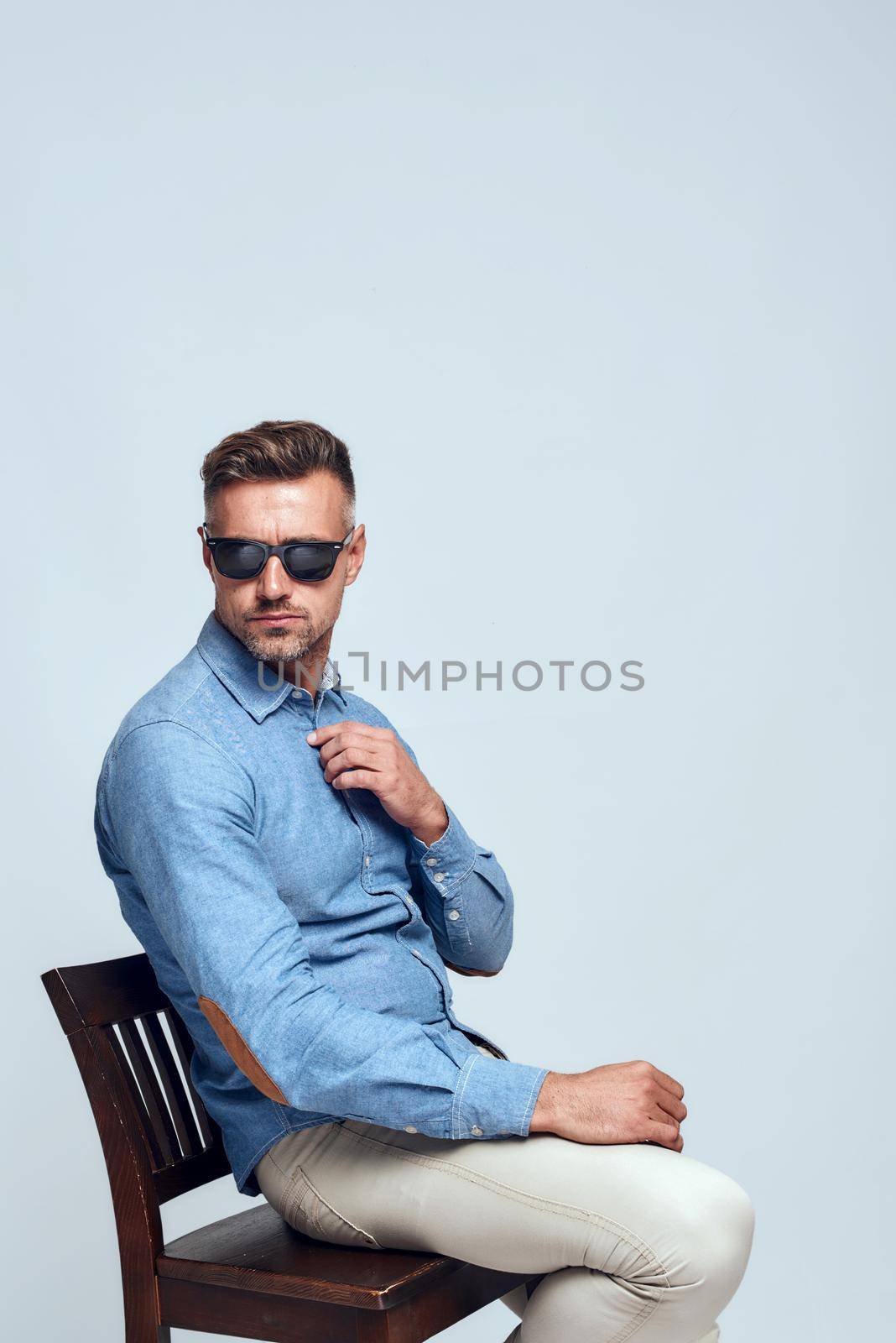 I need to think. Side view of serious bearded man in casual clothes and eyewear adjusting his shirt while sitting on the chair against grey background by friendsstock