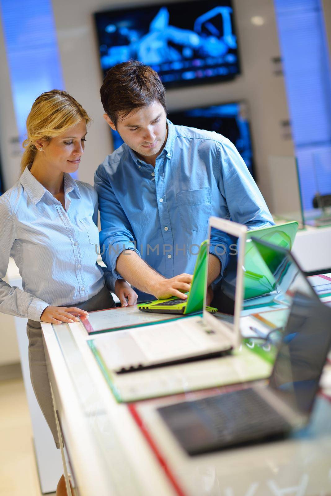 Young couple in consumer electronics store looking at latest laptop, television and photo camera