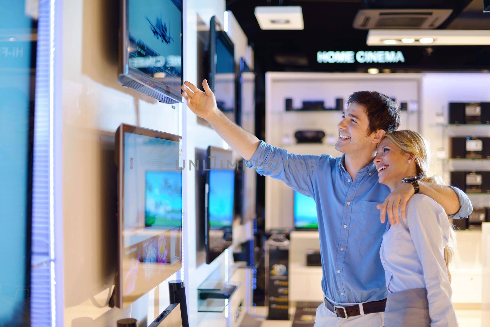 Young couple in consumer electronics store looking at latest laptop, television and photo camera