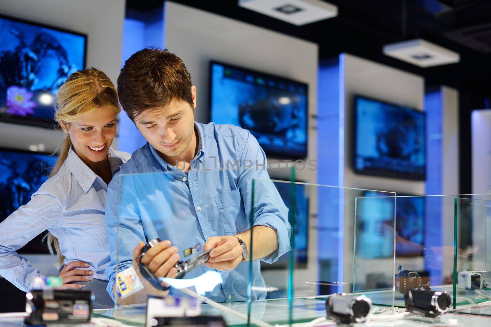 Young couple in consumer electronics store looking at latest laptop, television and photo camera