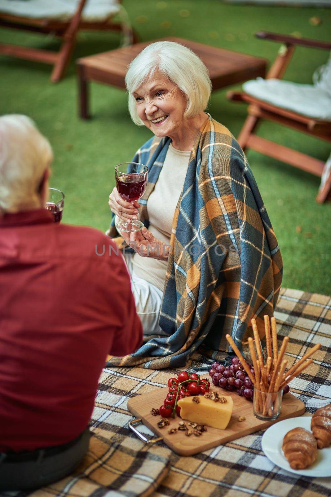 Happy elderly woman talking with her husband and holding wine by friendsstock
