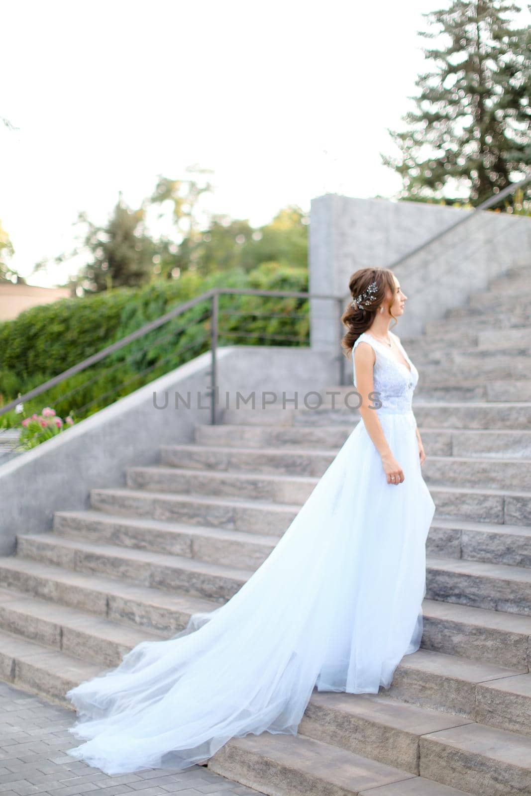 Back view of european bride walking on concrete stairs and wearing white dress. by sisterspro