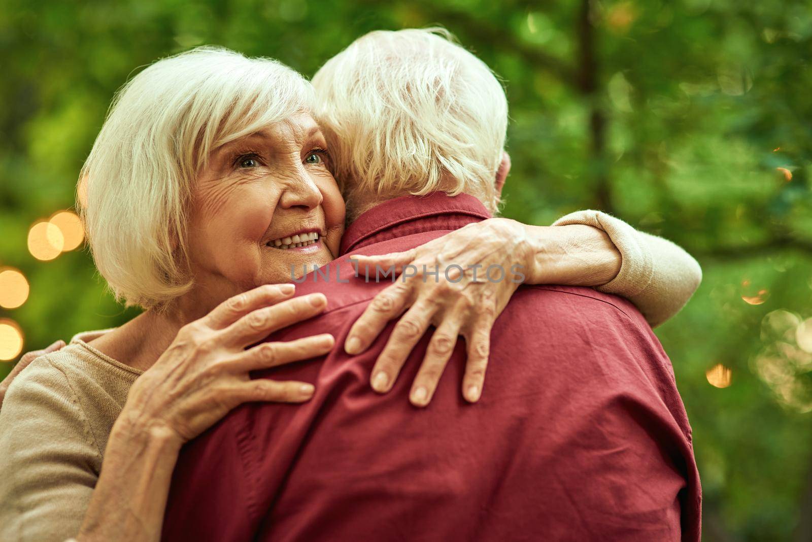 Waist up of smiling elderly lady hugging her spouse while spending time in the garden. Family concept