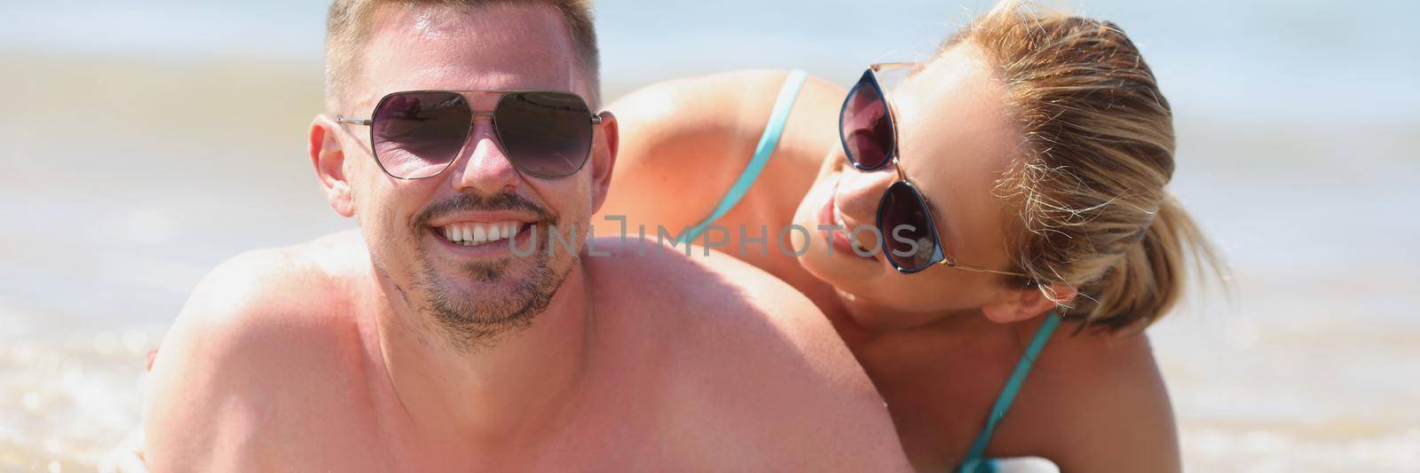 Young happy man and woman in sunglasses lying on seashore. Honeymoon concept