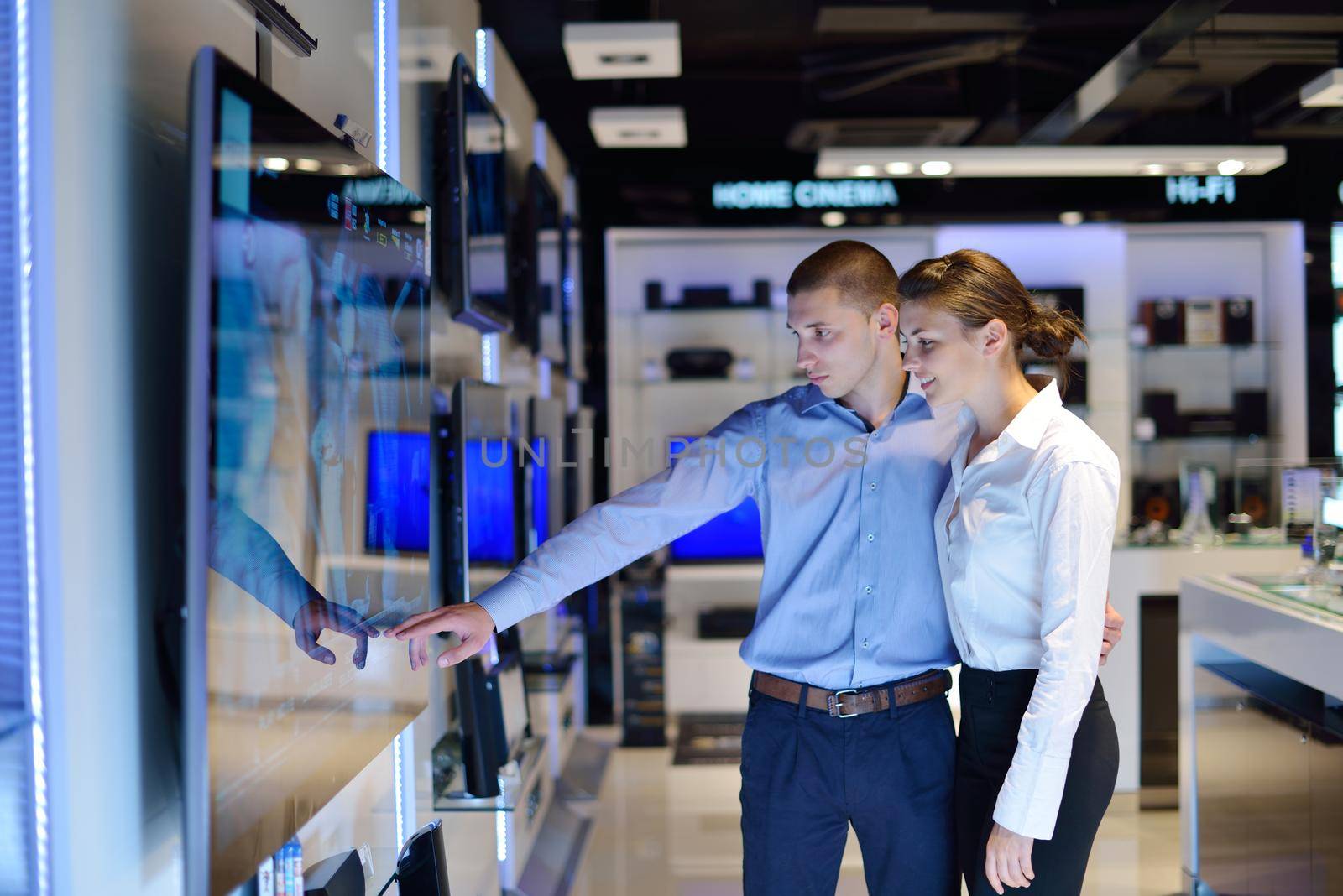 Young couple in consumer electronics store looking at latest laptop, television and photo camera to buy