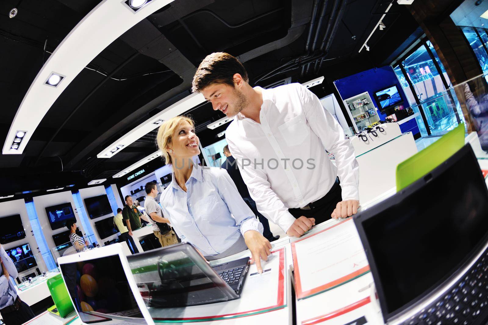 Young couple in consumer electronics store looking at latest laptop, television and photo camera