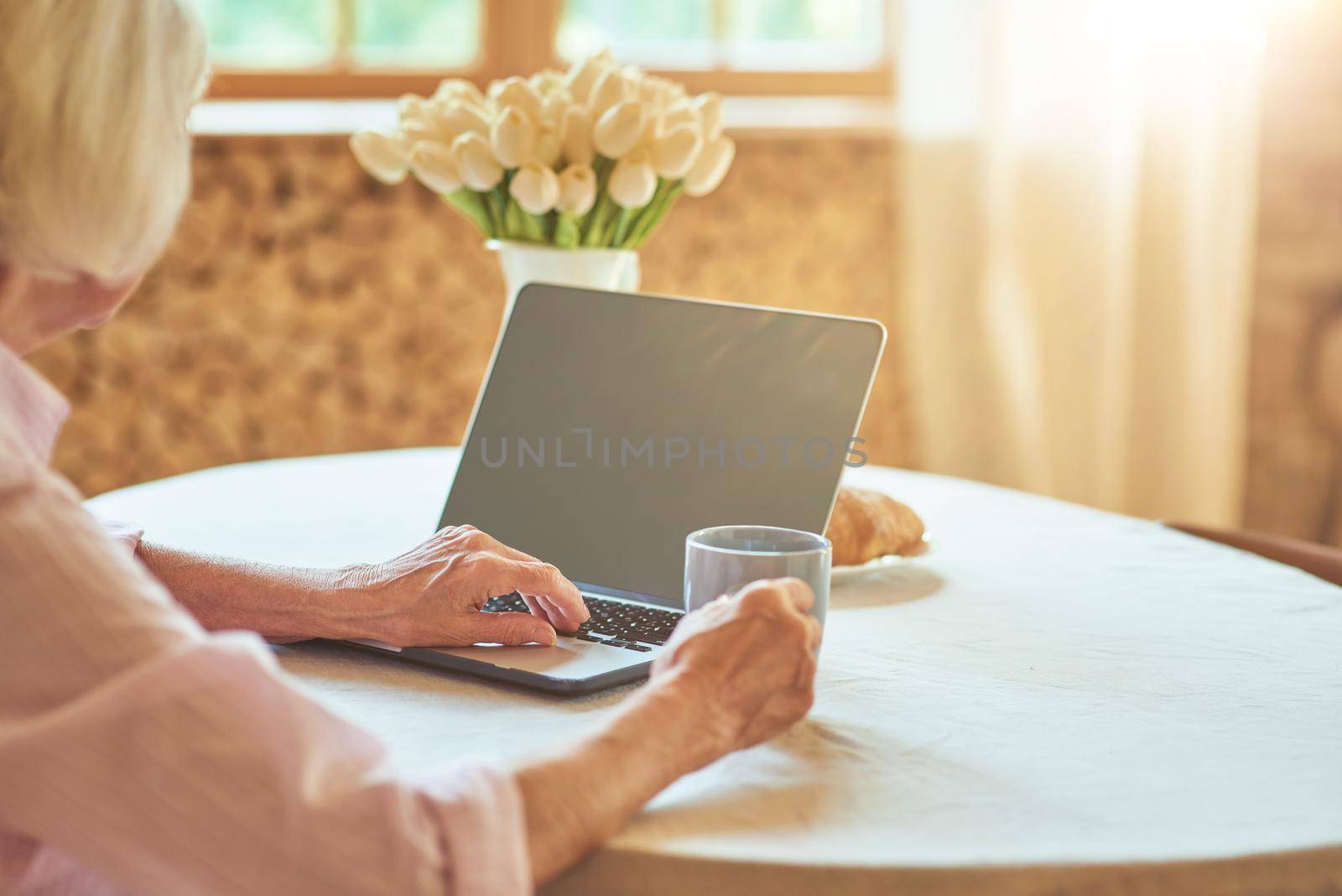 Elderly lady typing on computer in the morning by friendsstock