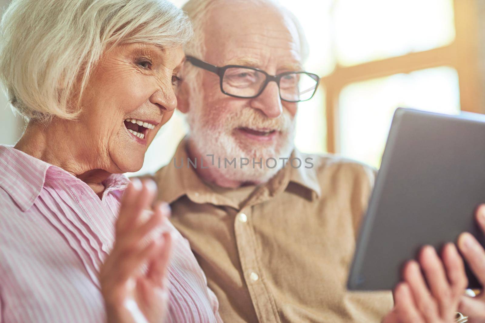 Close up of happy senior husband and wife using digital tablet and chatting during video call at home. Lifestyle concept