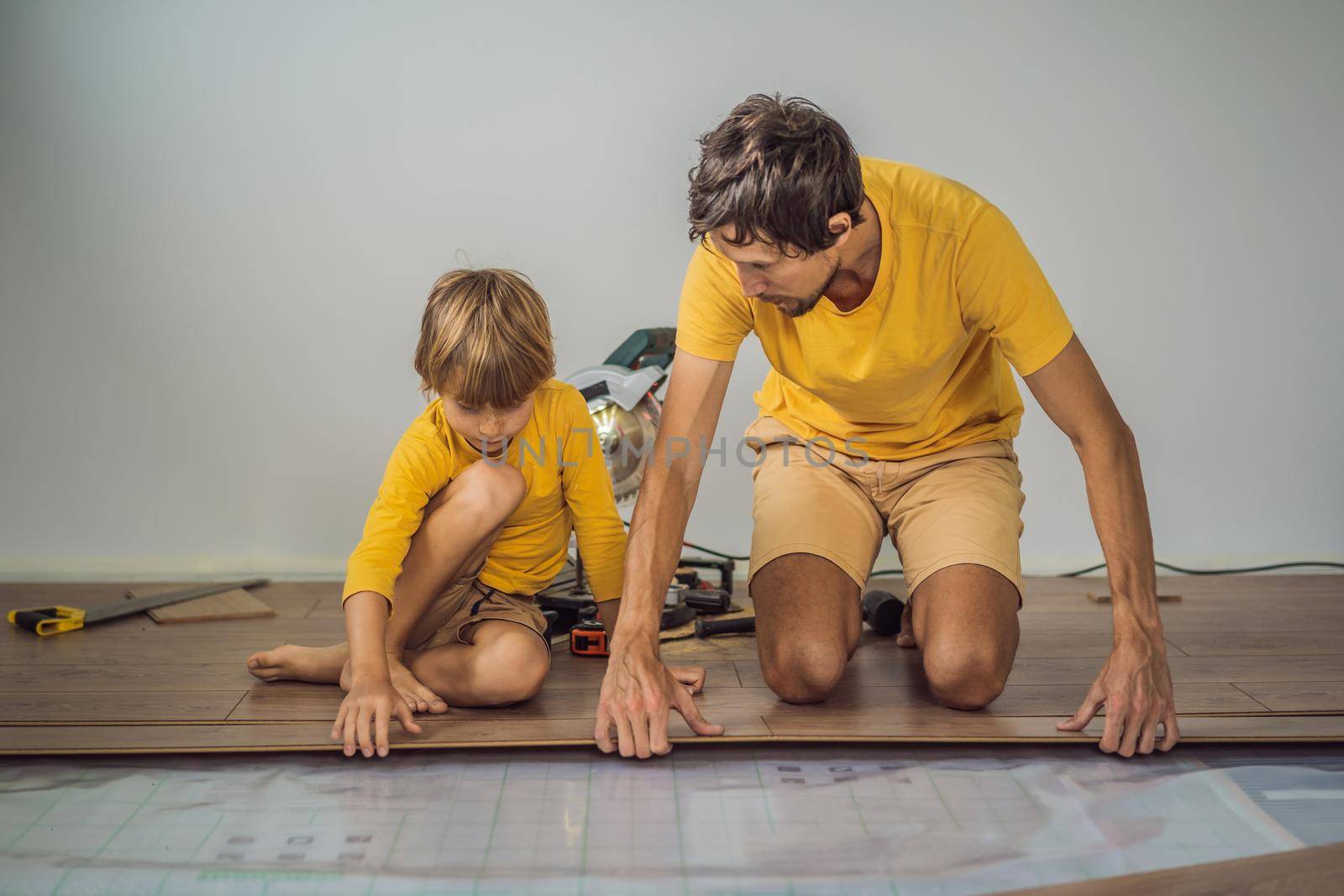Father and son installing new wooden laminate flooring on a warm film floor. Infrared floor heating system under laminate floor.