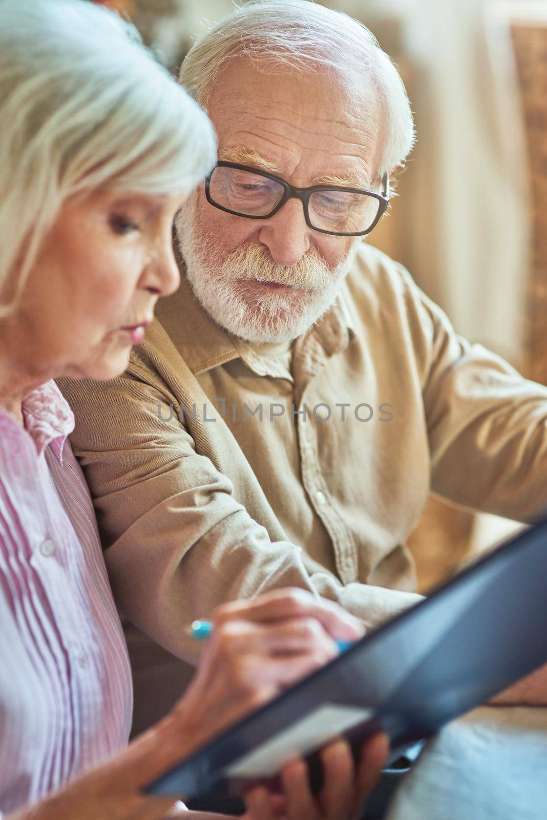Cropped photo of serious worried senior couple calculating bills to pay while sitting at home. Family and household concept