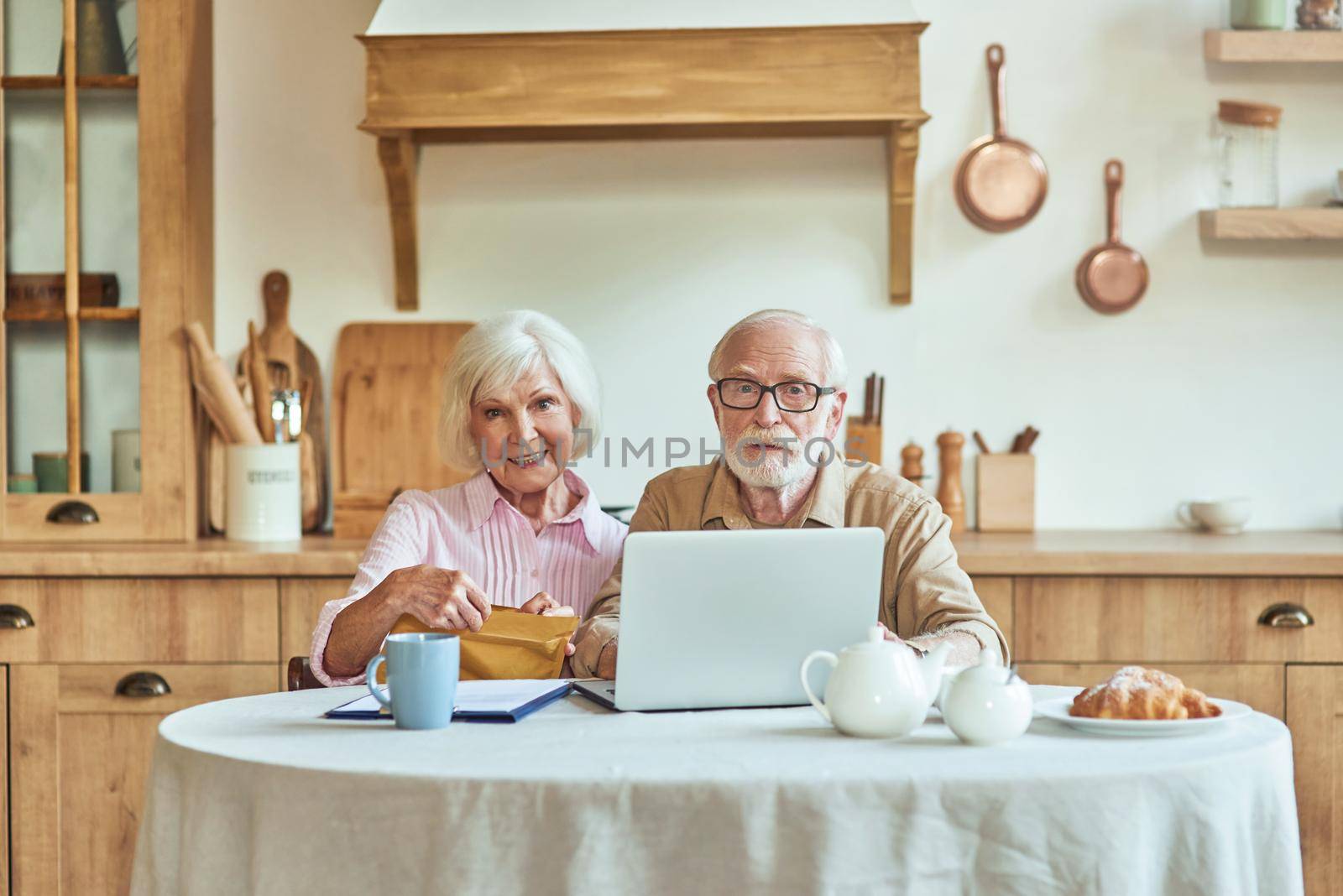 Elderly couple sitting at table while working with laptop and household document pay bills. Family and household concept