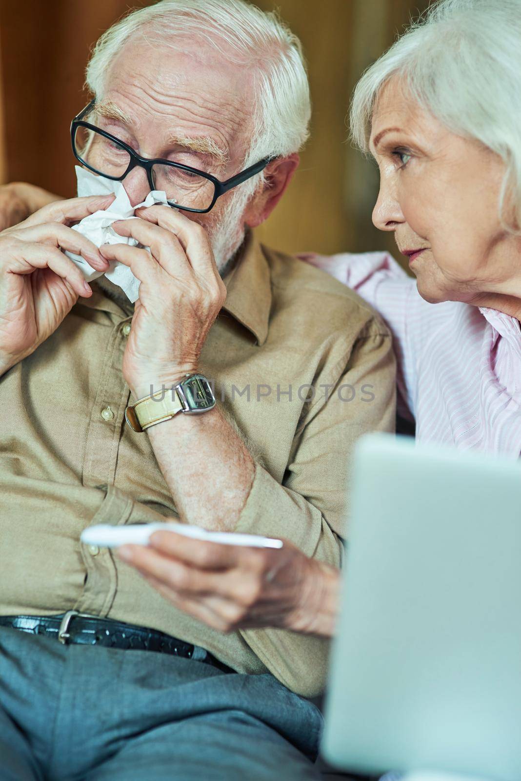 Sick elderly man checking temperature while his wife supporting him by friendsstock