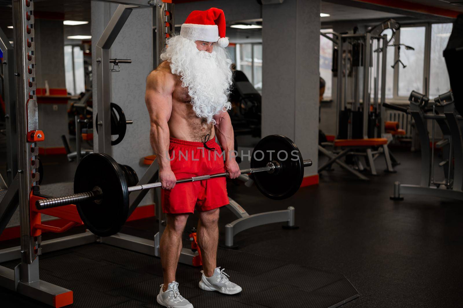 Santa claus in the gym. Muscular man with a naked torso doing exercises with dumbbells. by mrwed54