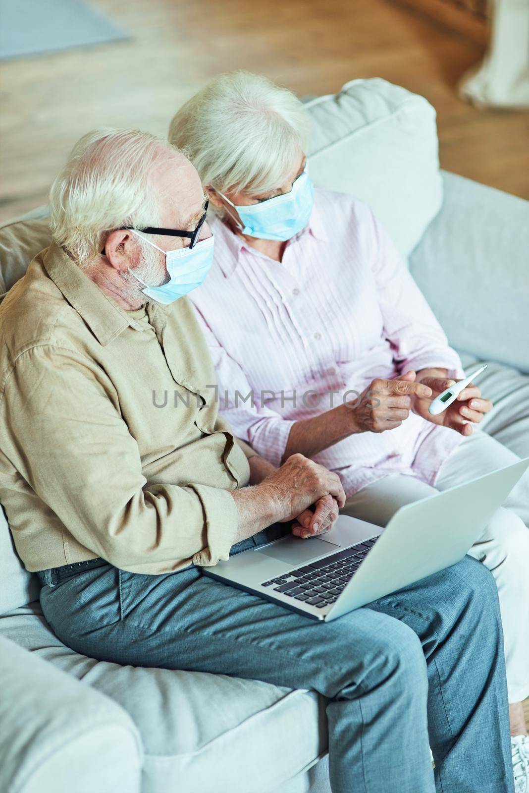 Top view of senior couple having online consultation with a doctor while using laptop and thermometer in living room. Care and health concept