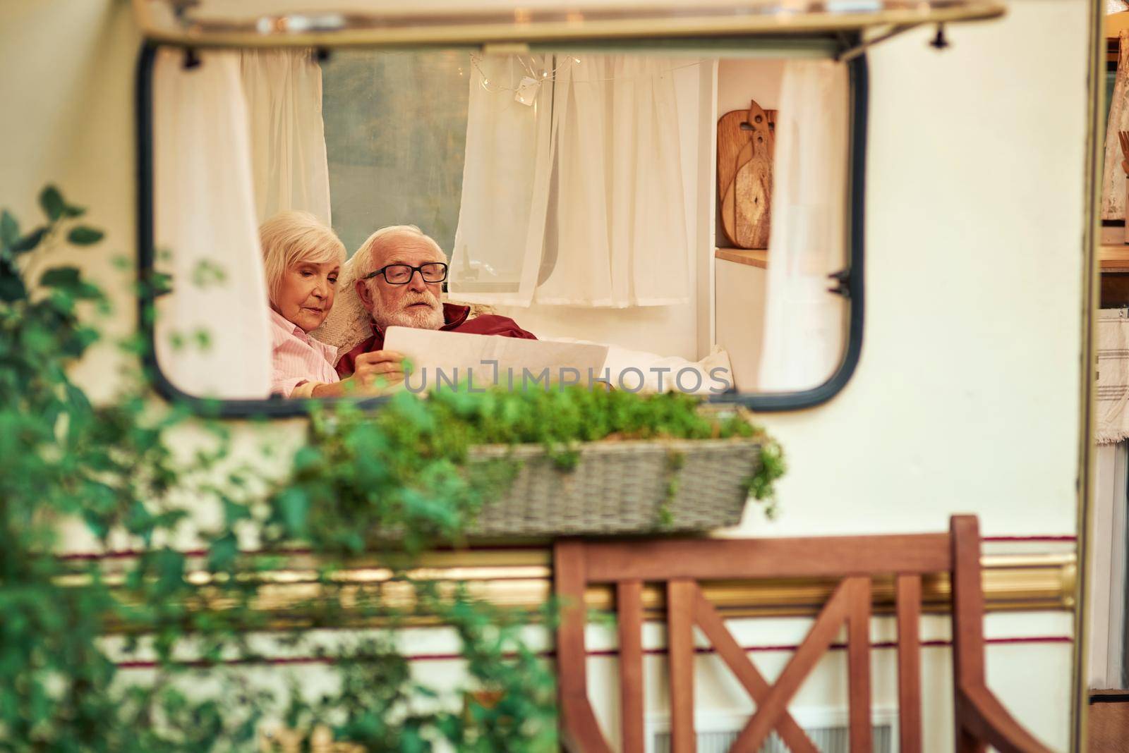 Senior couple carefully looking at the new route on the map while relaxing in their camper van. Travel concept