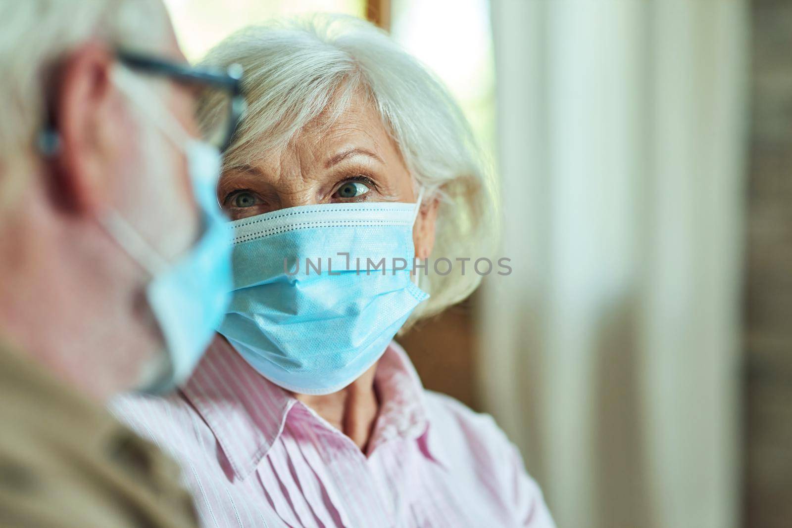 Cropped photo of senior woman looking at her husband while wearing protective masks at home. Care and health concept