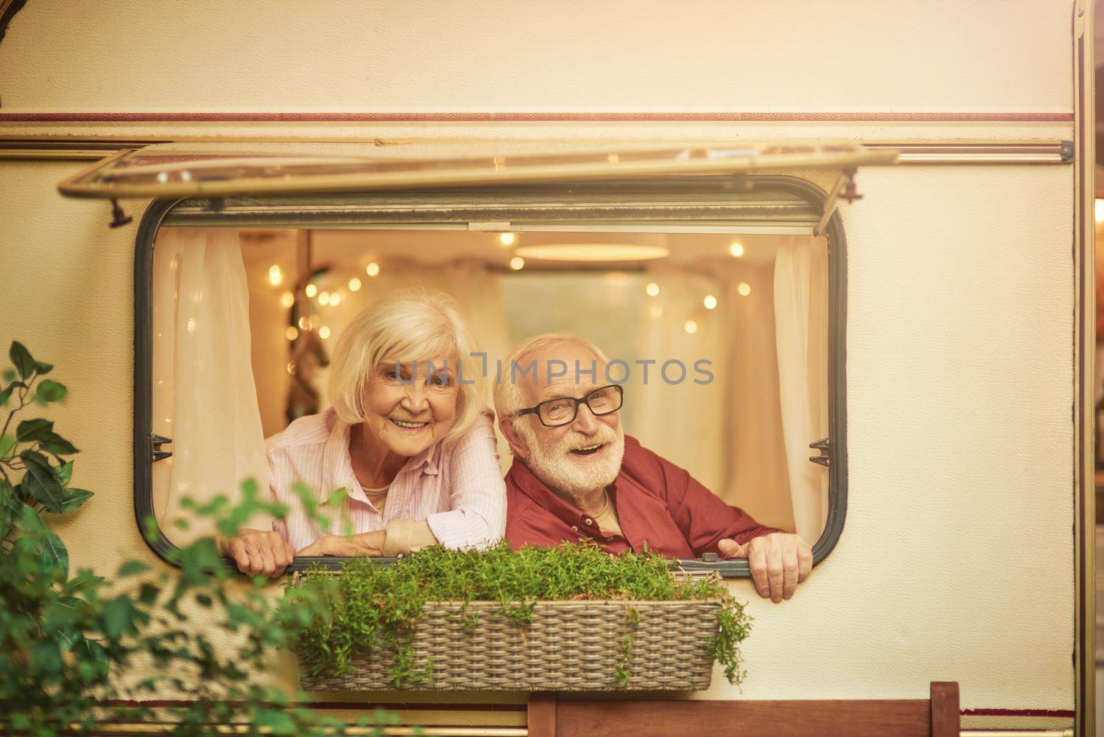 Happy elderly couple resting in their camper van while looking out the window. Travel and lifestyle concept