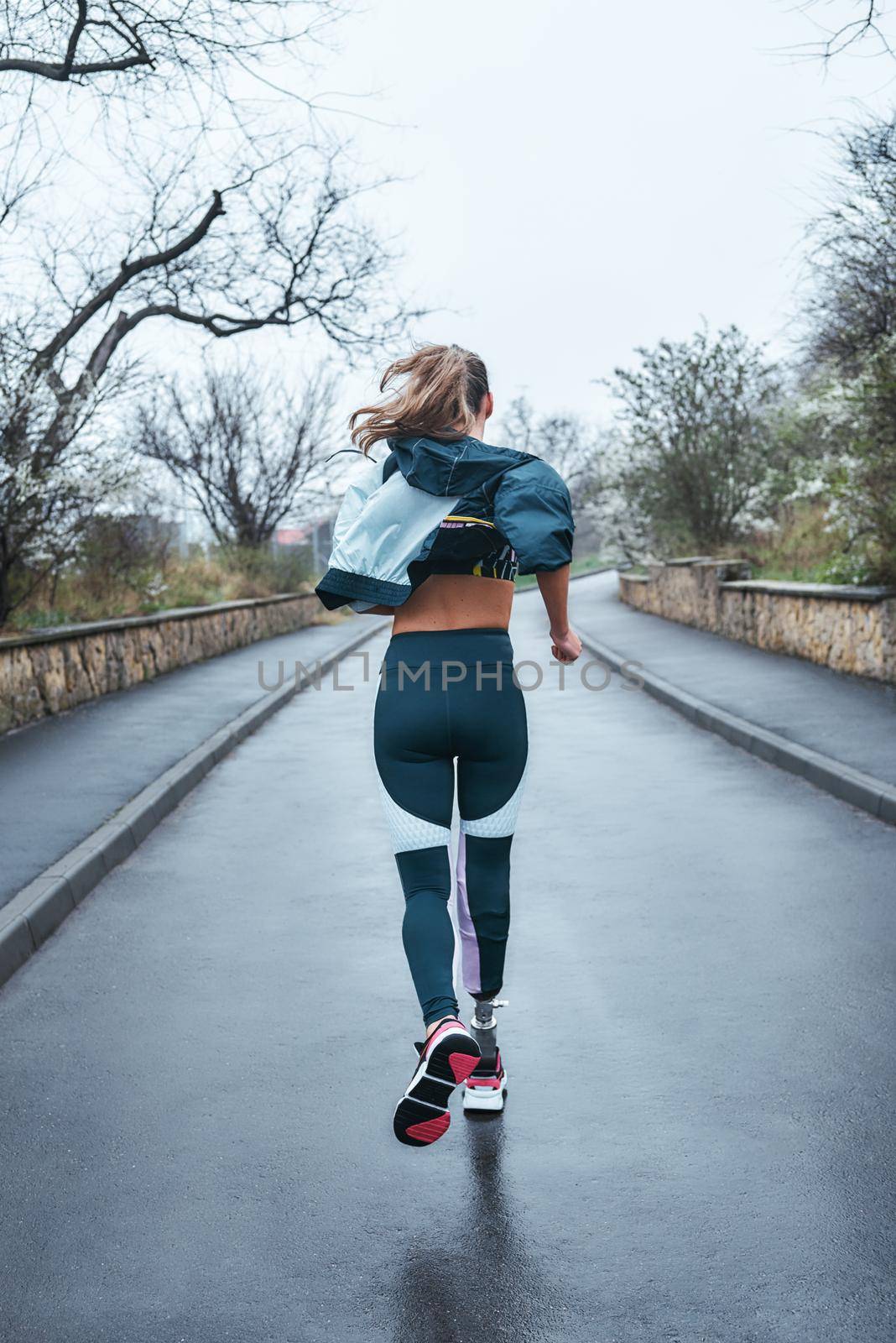You can do it Back view of strong disabled woman with bionic leg in sportswear is running outdoors by friendsstock
