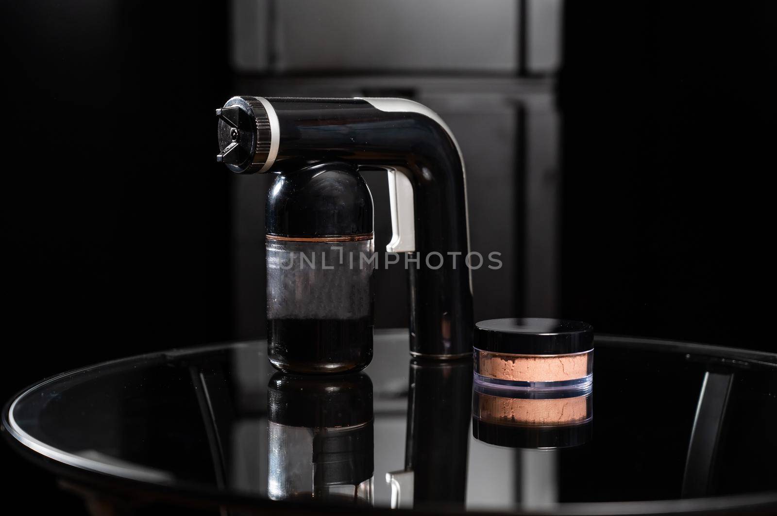 A close-up of the instant tanning equipment. Gun spraying paint for leather and matting body powder on a black background.