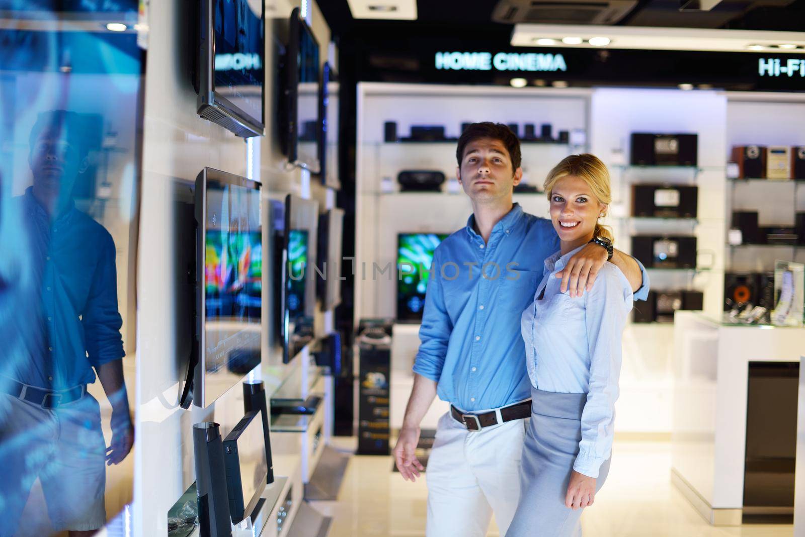 Young couple in consumer electronics store looking at latest laptop, television and photo camera