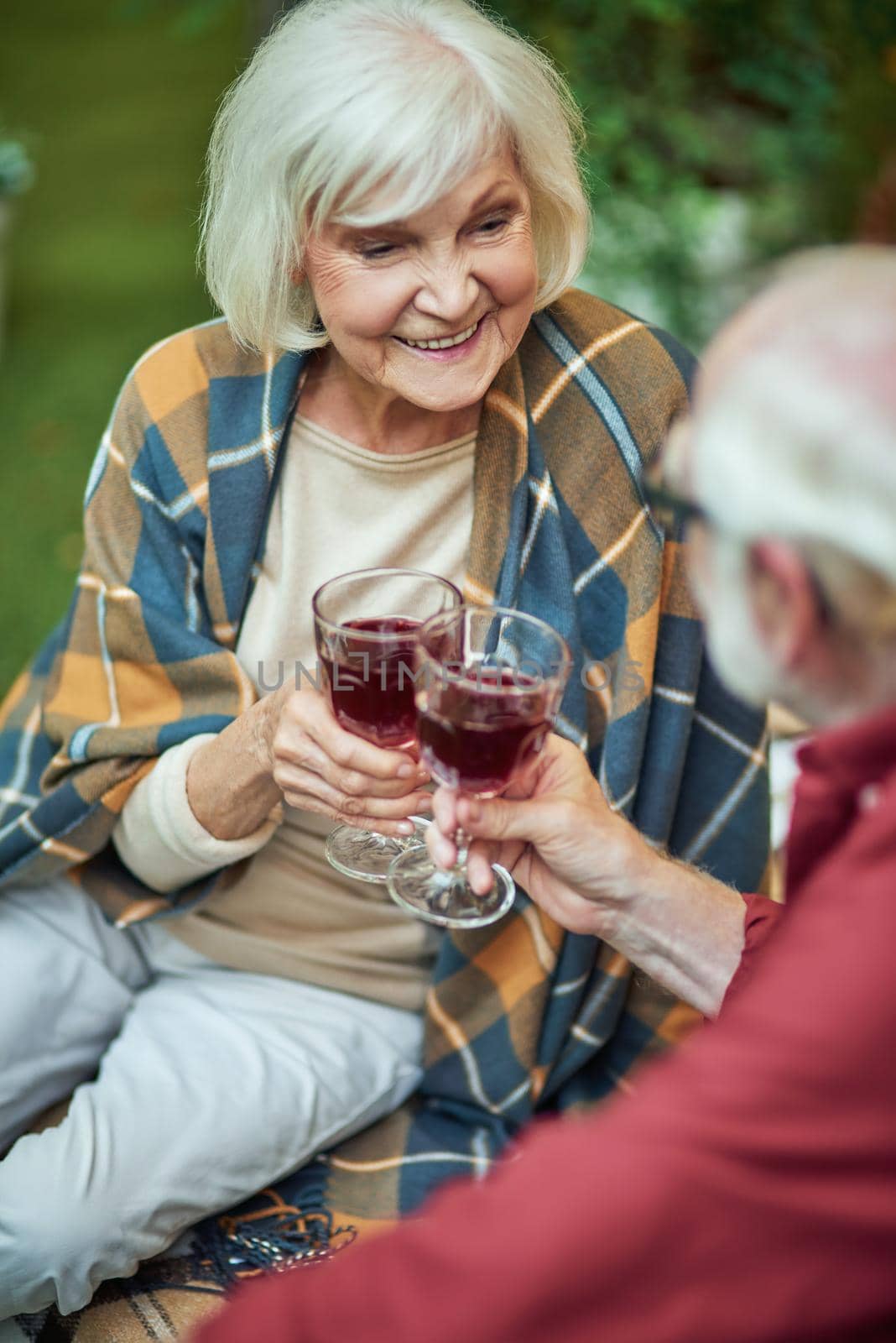 Happy beautiful lady sitting next to her husband while holding glasses with red wine outdoors. Relationship and family concept