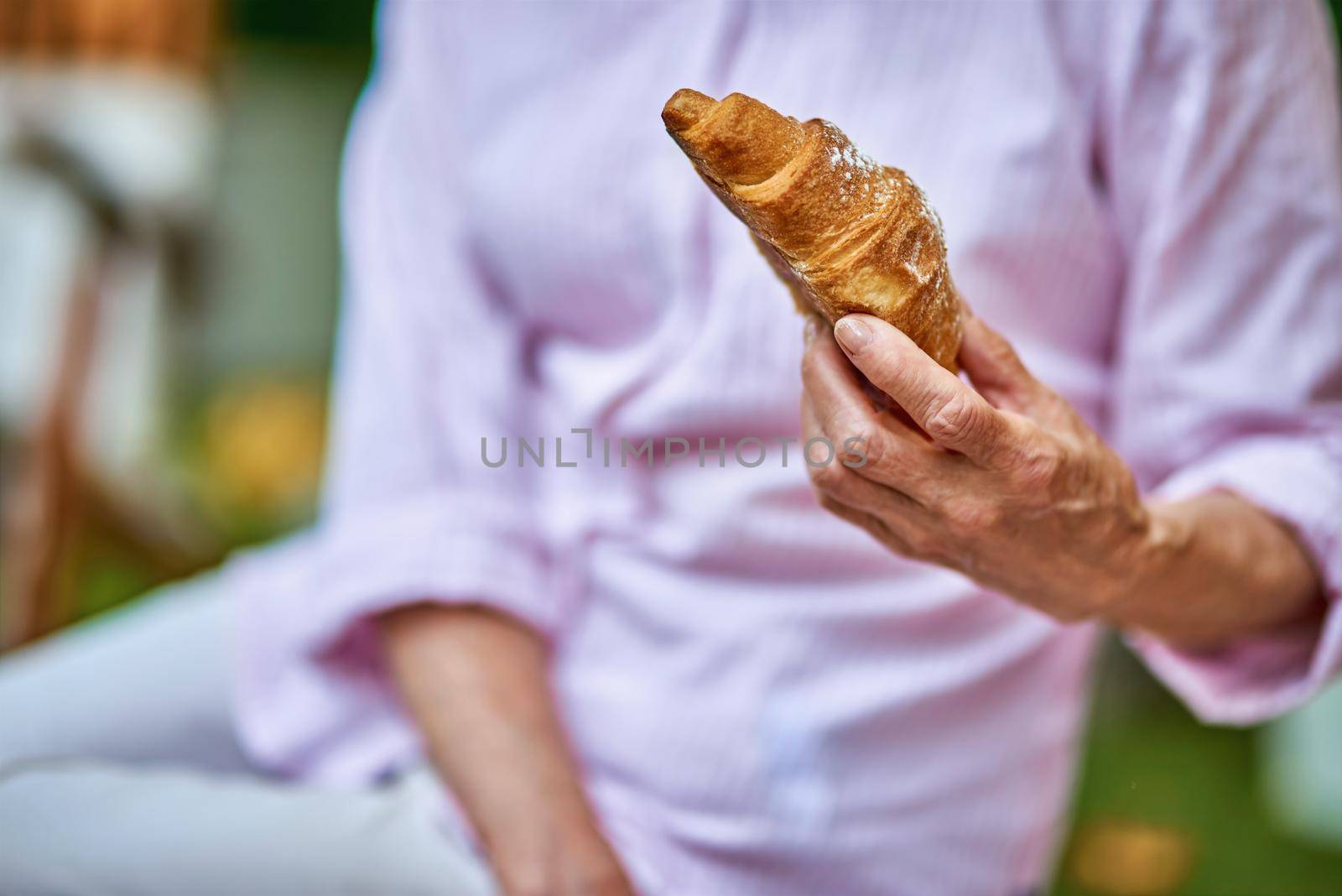 Cropped photo of female hand holding croissant during a picnic. Lifestyle and food concept