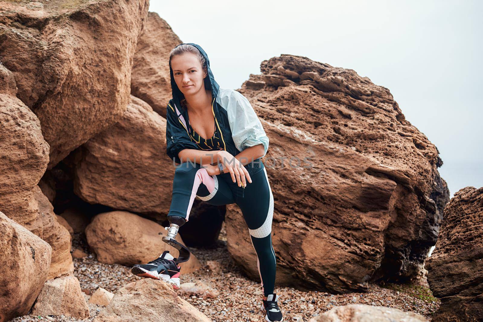 Never give up Beautiful and young disabled athlete woman in sportswear with prosthetic leg standing on the beach after morning workout and looking at camera by friendsstock