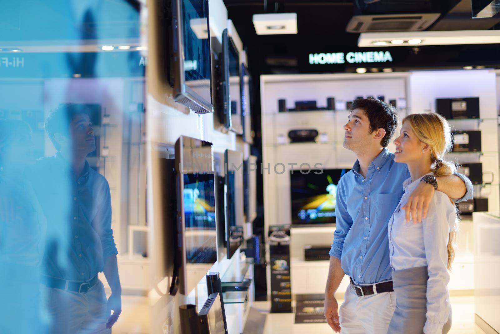 Young couple in consumer electronics store looking at latest laptop, television and photo camera