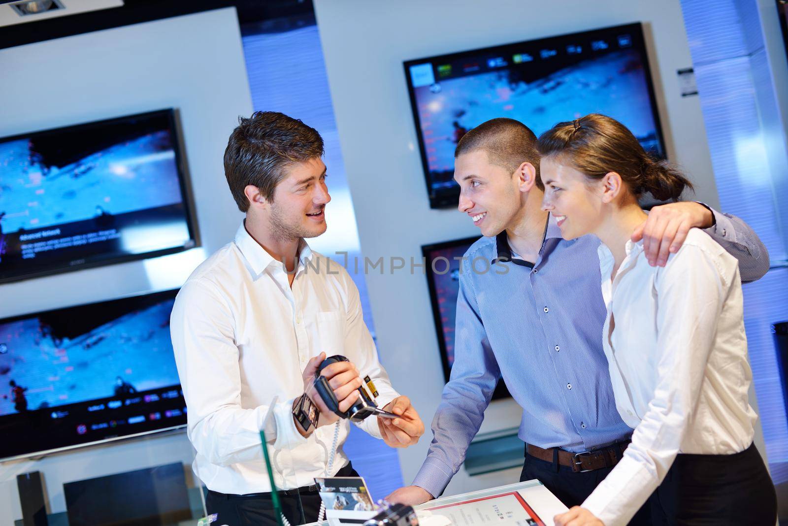 Young couple in consumer electronics store looking at latest laptop, television and photo camera to buy