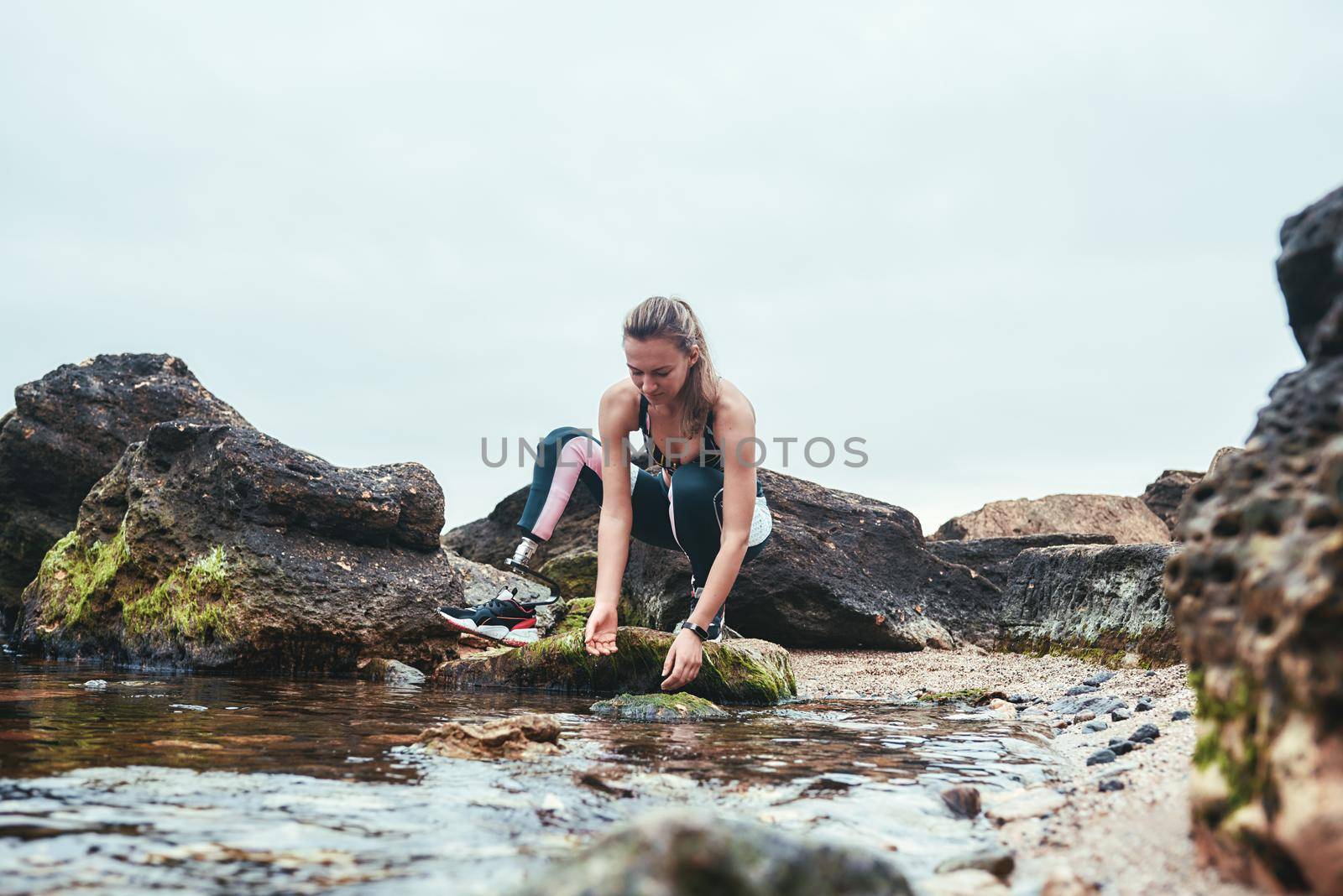 Woman in sportswear with prosthetic leg taking water in her hand from the river by friendsstock