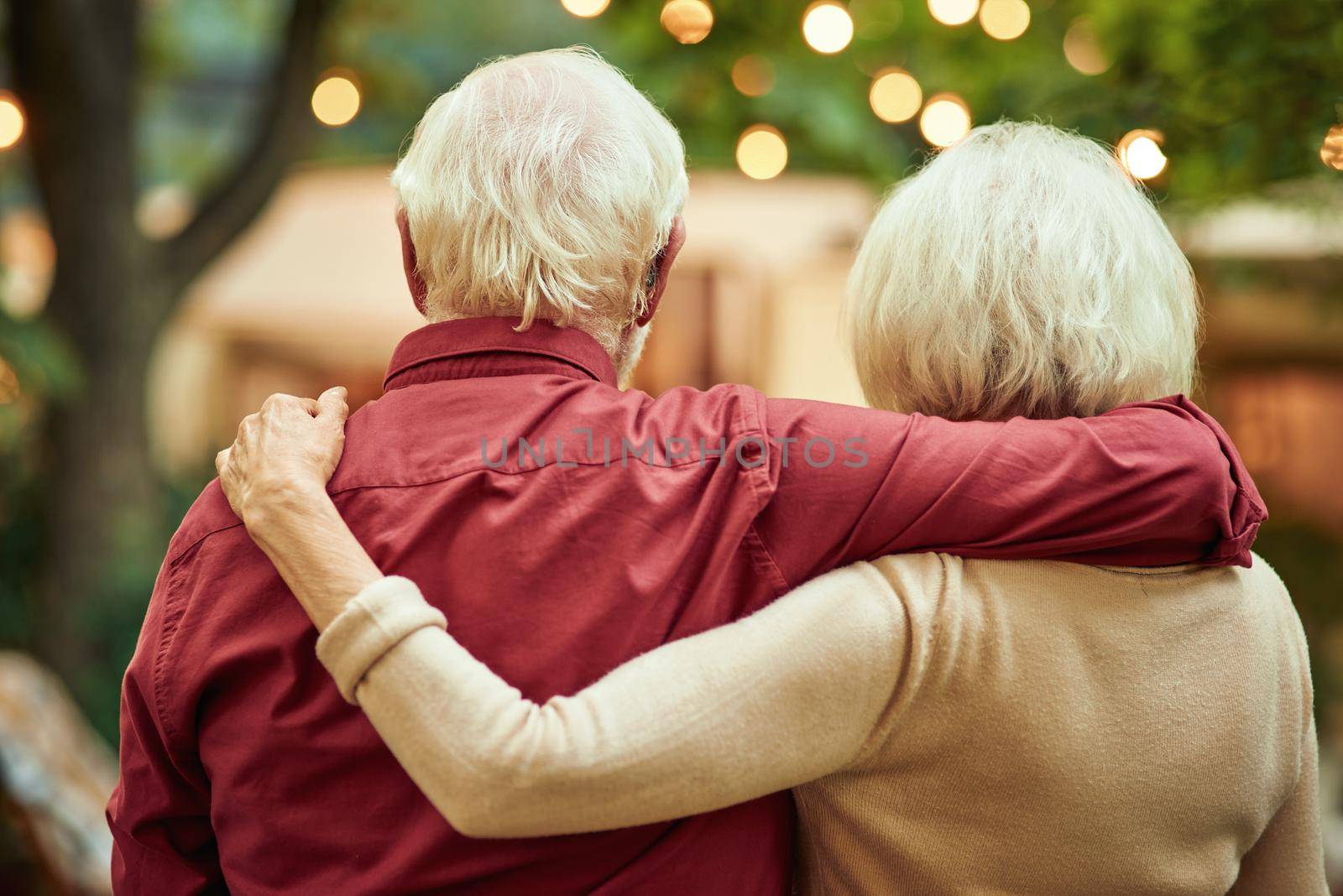 Waist up of senior couple hugging and looking at their camper van while enjoying the evening. Travel and lifestyle concept