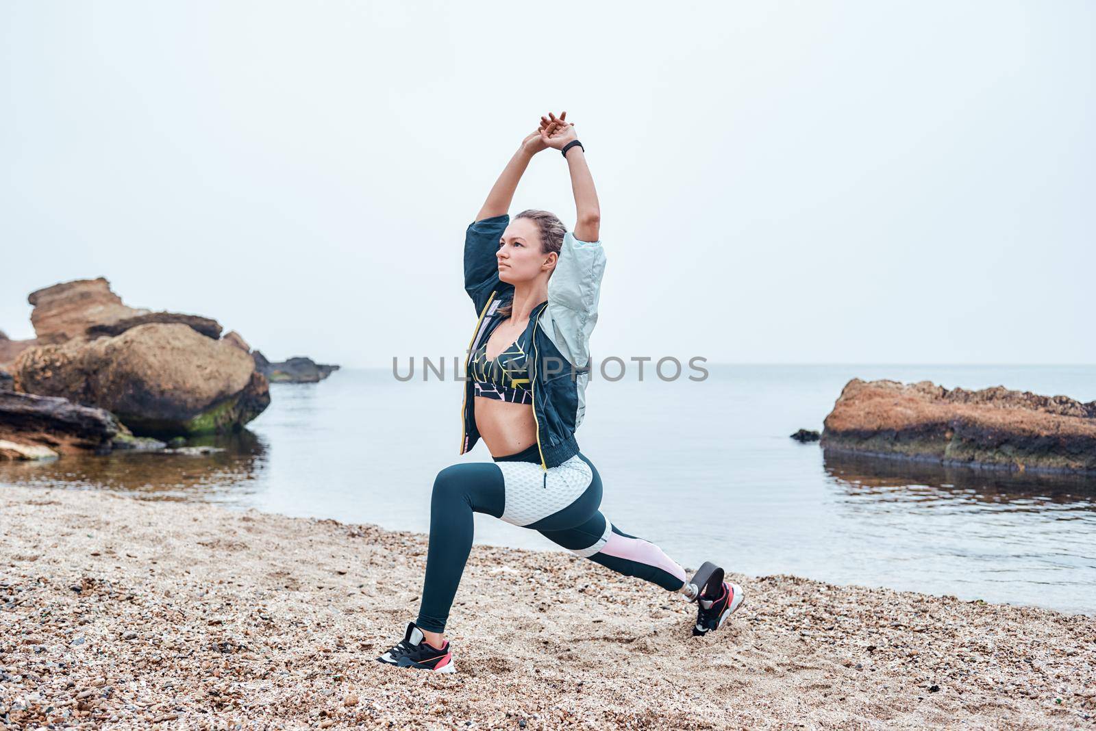 Sea Inspiration. Amazing disabled athlete woman in sportswear with prosthetic leg standing in yoga pose at the beach. Sport concept. Disabled Sportsman. Healthy lifestyle